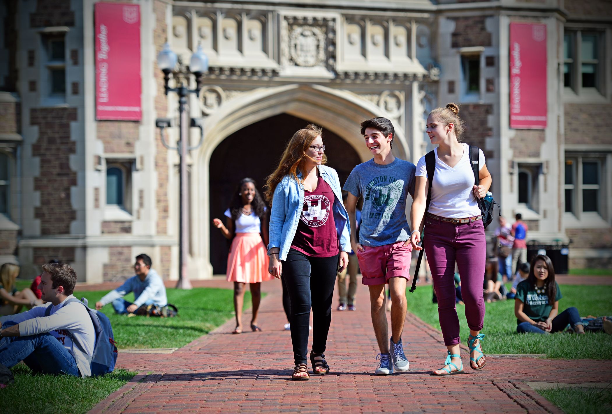 Three students walking along a brick path outside of Brookings Hall on WashU's campus. 