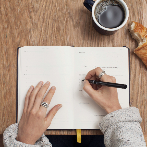 woman writing in notebook, cup of coffee and crossaint nearby