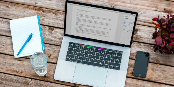 laptop resting on wooden table with open notebook beside it