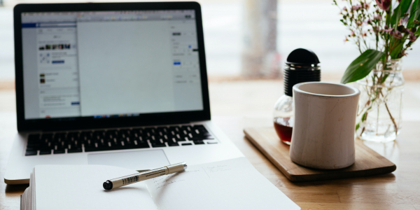 notebook laying open on a table with laptop on in the background