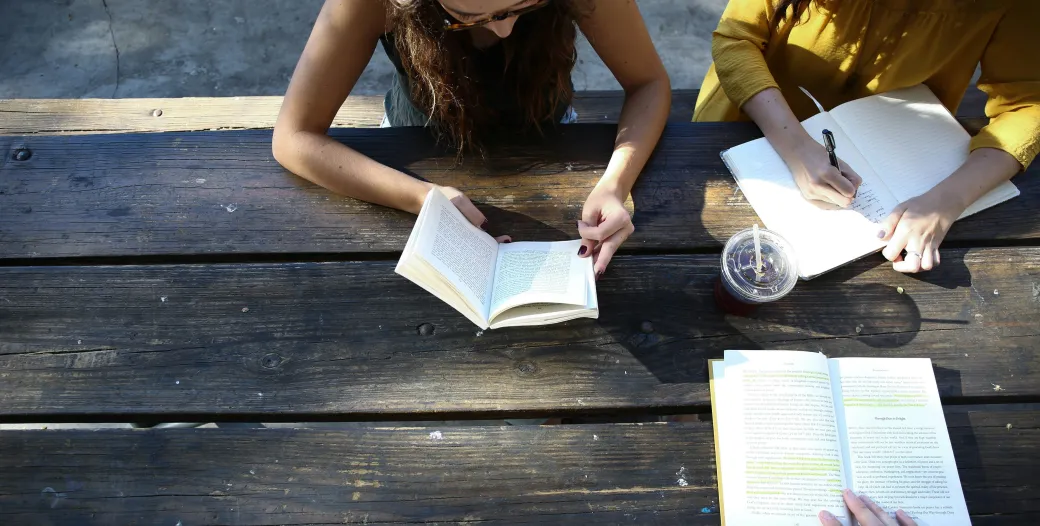 students sitting outside at table with books open